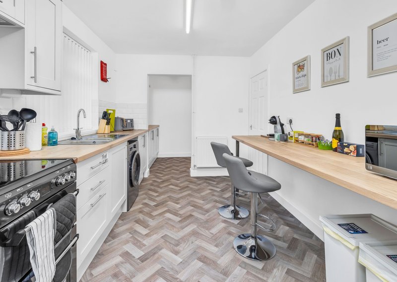Modern galley kitchen with white cabinetry, wooden countertops, herringbone flooring and bar seating