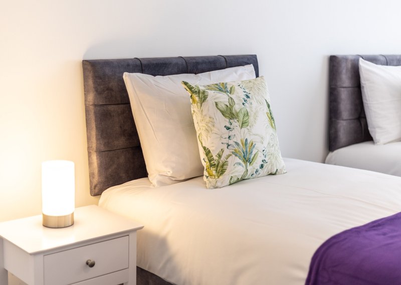 Modern bedroom with double bed, decorative pillows, bedside lamp and white nightstand
