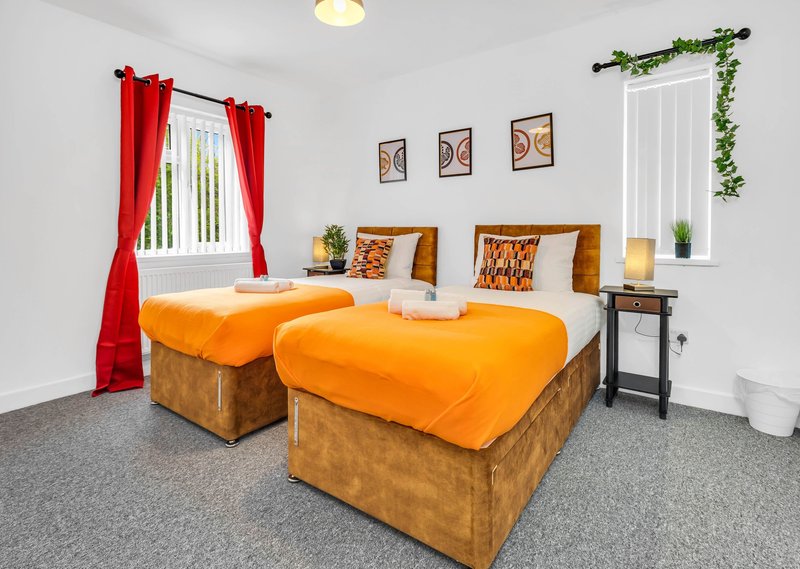 Bright bedroom with two single beds, orange bedding, red curtains and white walls