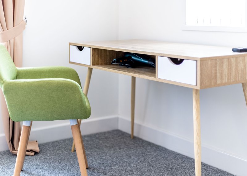Modern workspace with wooden desk, green upholstered chair, and white walls
