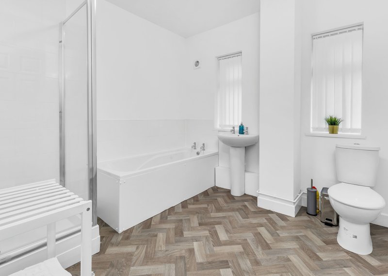 Clean bathroom with shower enclosure, white bathtub, pedestal sink, toilet and herringbone floor
