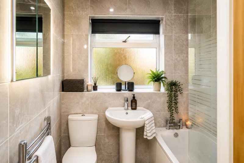 Modern bathroom with pedestal sink, toilet, bathtub and window with frosted glass