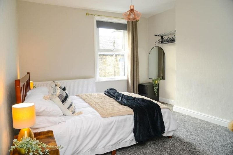 Bedroom with double bed, white bedding, dark throw, wooden headboard and pendant light