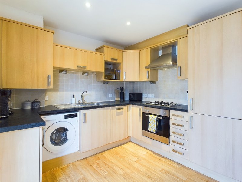 Modern kitchen with light wood cabinets, integrated appliances, black countertops and wooden flooring