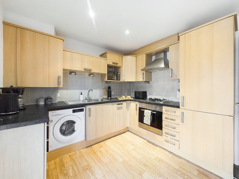 Modern kitchen with light wood cabinets, black countertops, integrated appliances and wooden flooring