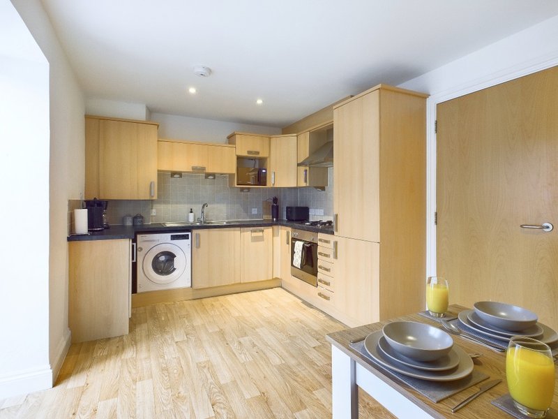 Modern kitchen with light wood cabinets, integrated appliances, and wooden flooring