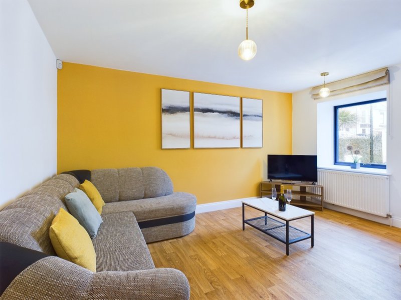 Bright living room with yellow walls, grey upholstered sofa, wooden floor and TV unit