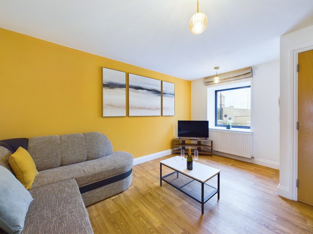 Bright modern living room with gray corner sofa, yellow accent wall, wooden floor and pendant light