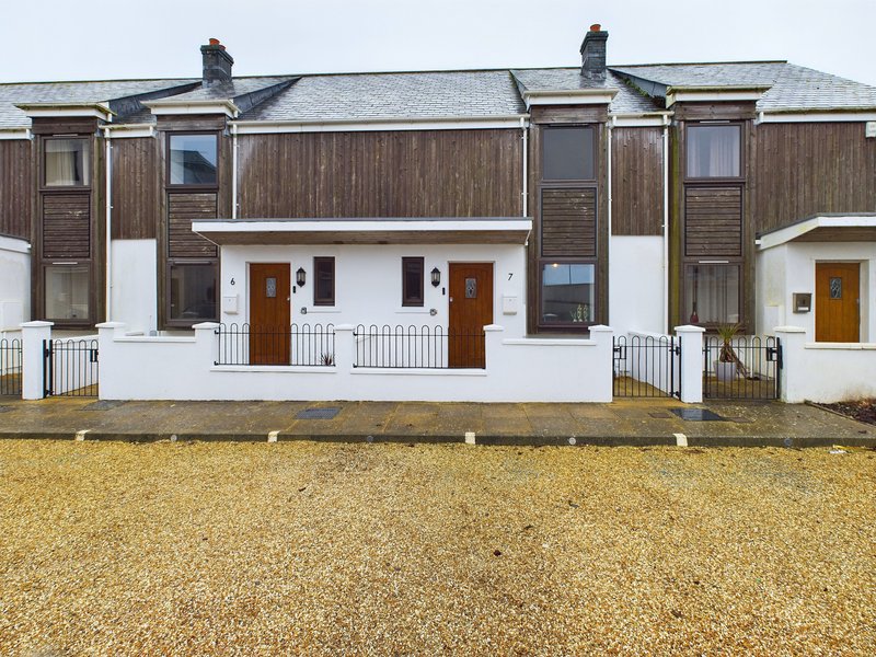 Row of traditional terraced houses with white porches, brown wooden cladding and gravel forecourt