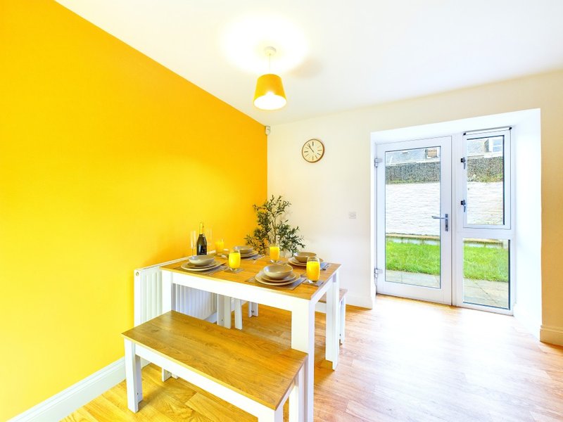 Bright dining area with yellow accent wall, white table, wooden bench and garden view