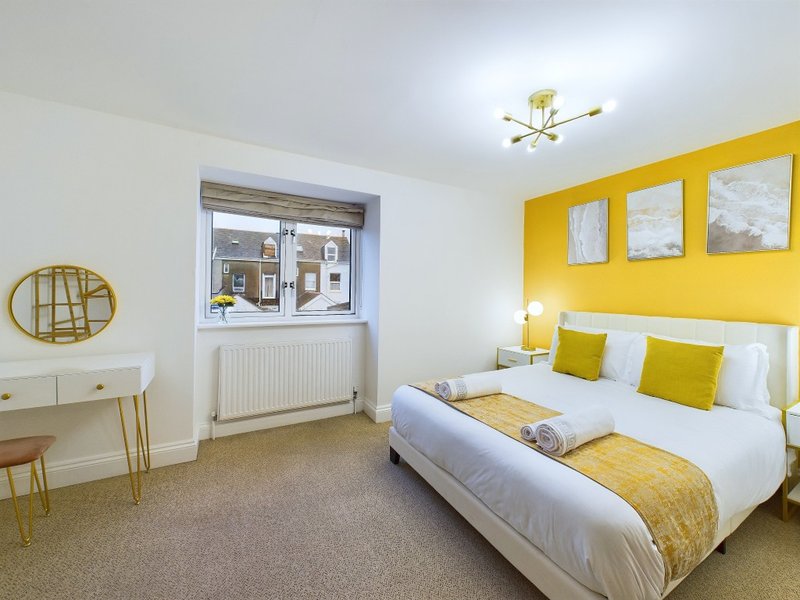 Bright bedroom with double bed, yellow accent wall, desk, window and neutral carpet