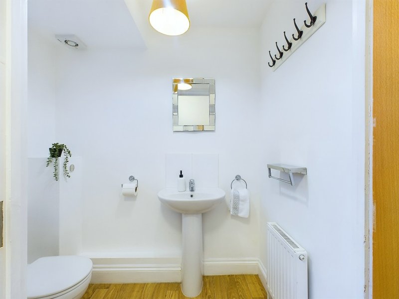 Small bathroom with pedestal sink, toilet, mirror and wooden flooring