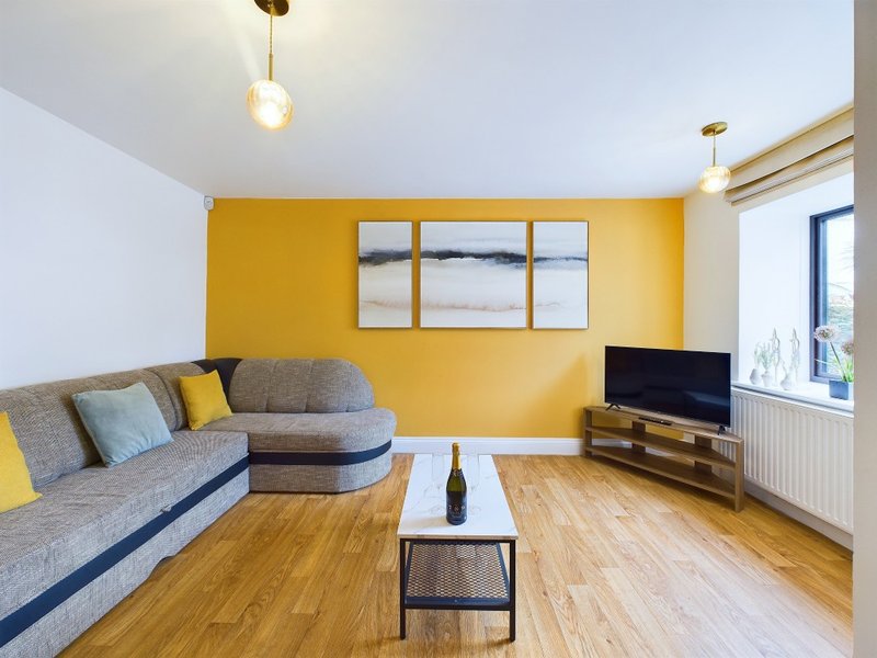 Modern living room with gray sofa, yellow accent wall, wooden floor and flat-screen TV
