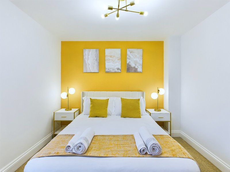 Modern bedroom with double bed, yellow accent wall, white bedding and matching pillows