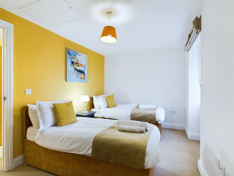 Bright bedroom with yellow walls, twin beds, gold pendant lamp and framed artwork
