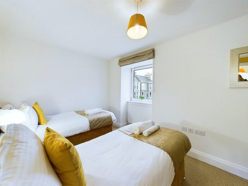 Bright bedroom with two single beds, gold cushions, pendant light and window view