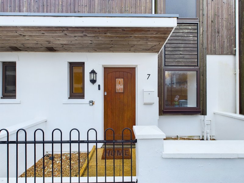 White cottage exterior with brown wooden door, metal gate, and small front entrance