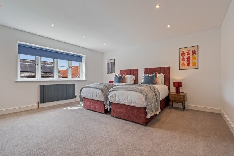 Spacious bedroom with two double beds, burgundy headboards, and large window overlooking rooftops