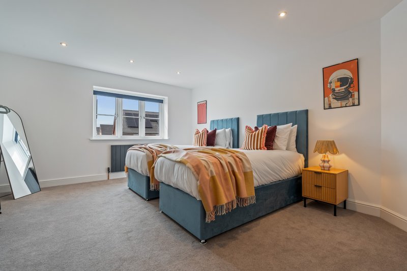 Modern bedroom with two single beds, blue headboards, warm bedding and wooden bedside table with lamp