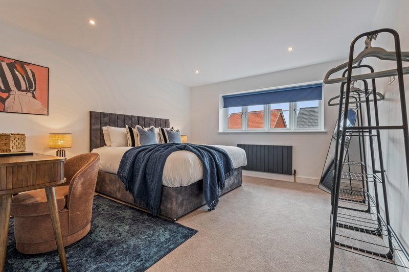 Spacious bedroom with double bed, wooden desk, chair, and towel rack by window