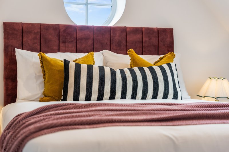 Modern bedroom with upholstered headboard, colorful pillows, striped cushion, and round window