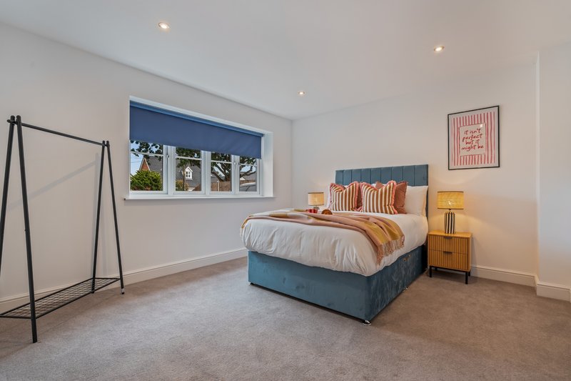 Modern bedroom with blue bed frame, striped pillows, wooden nightstand, and large window