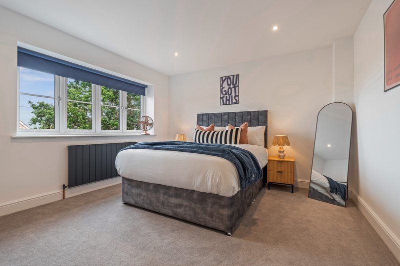 Bright modern bedroom with double bed, wooden nightstand, mirror, and large window