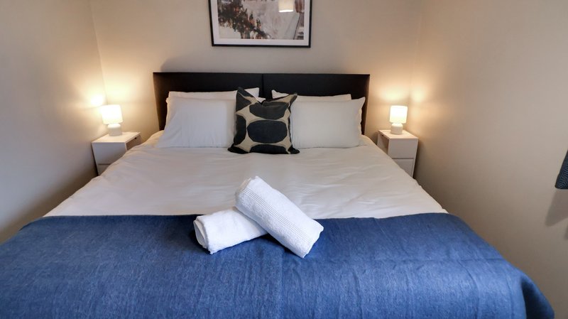 Modern bedroom with double bed, blue throw, white pillows, black headboard and bedside lamps