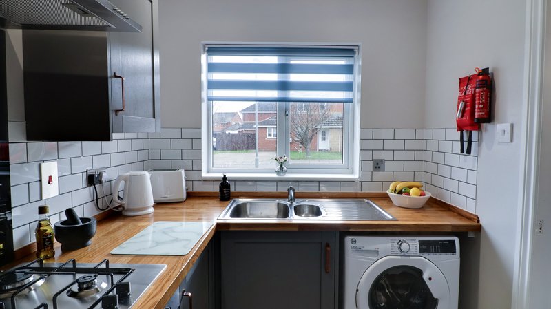 Modern kitchen with wooden countertops, sink, washing machine and window with blinds