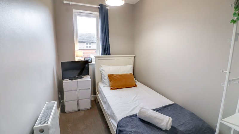 Compact bedroom with single bed, small TV unit, window with curtains and bedside storage