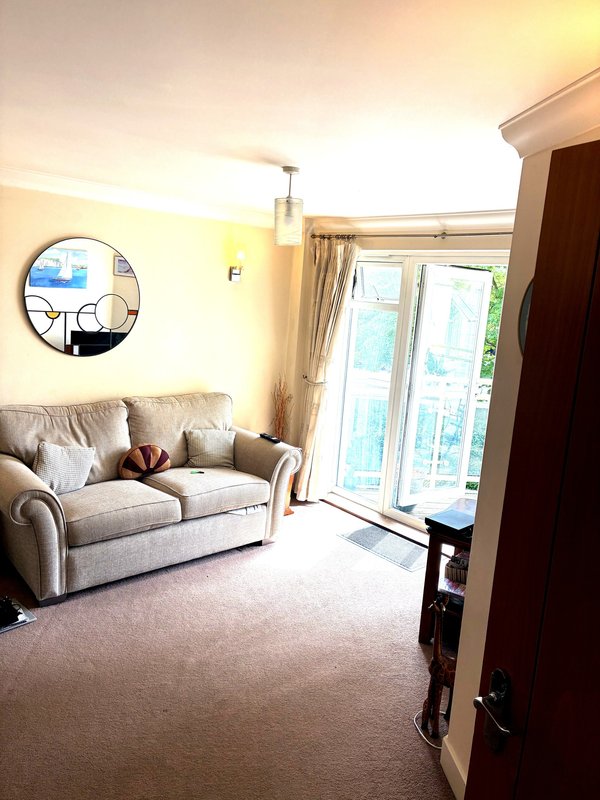 Bright living room with beige sofa, round mirror, and glass patio doors opening to garden
