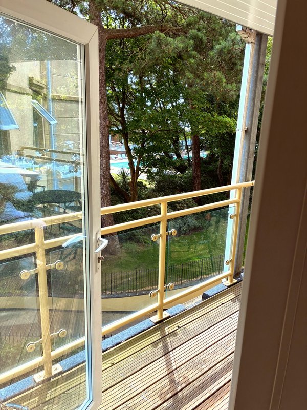 Sliding glass door opening to wooden deck with metal railing and tree views