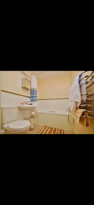 Small bathroom with toilet, sink, bathtub, towel rack and striped rug