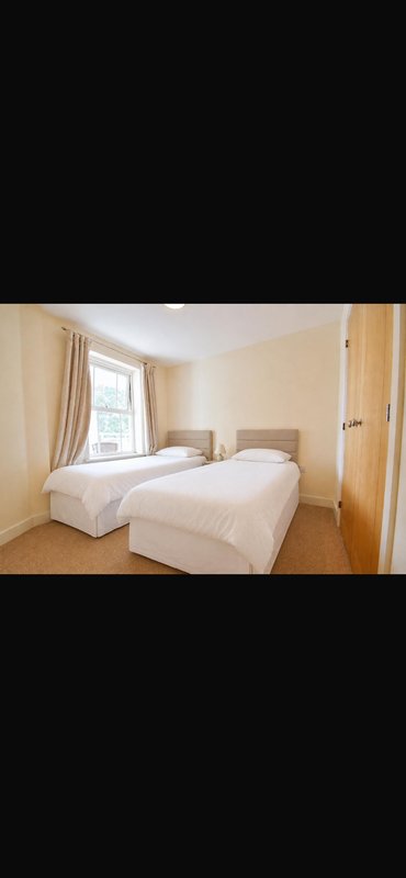Bright bedroom with two single beds, wooden floor, window with curtains and door