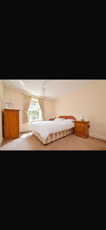 Spacious bedroom with double bed, wooden furniture, window and carpet flooring