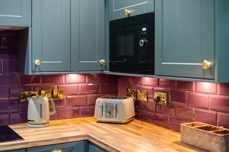 Modern kitchen with teal cabinets, red brick backsplash, wooden countertop and appliances