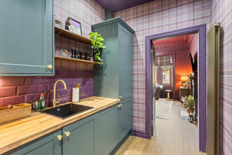 Modern kitchen with teal cabinetry, purple tile backsplash, wooden countertop and open doorway