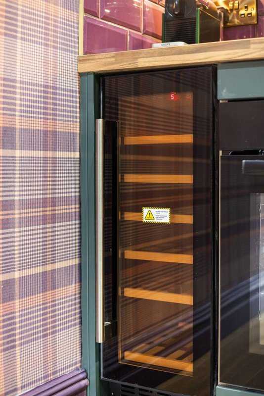 Kitchen area with black glass-door wine refrigerator, wooden counter, and checkered wall panel