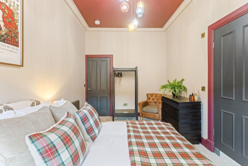 Bedroom with double bed, tartan bedding, black dresser, plant, and colored ceiling