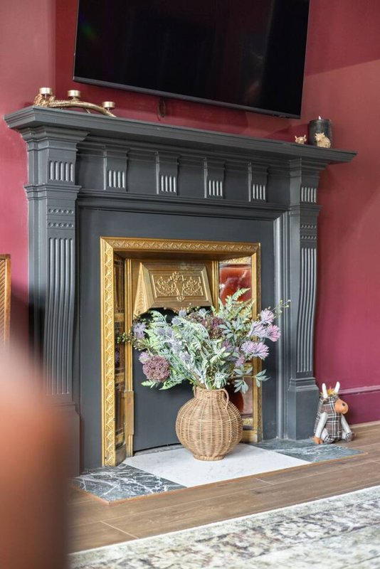 Fireplace with grey surround, gold frame, fresh flowers in vase, TV mounted above