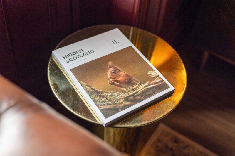 Gold side table with magazine featuring bird cover and decorative plate