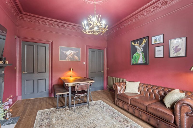 Pink living room with brown leather sofa, framed artwork, pendant light, and wooden flooring