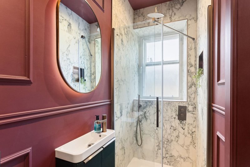 Modern bathroom with burgundy walls, round mirror, marble shower enclosure and white sink