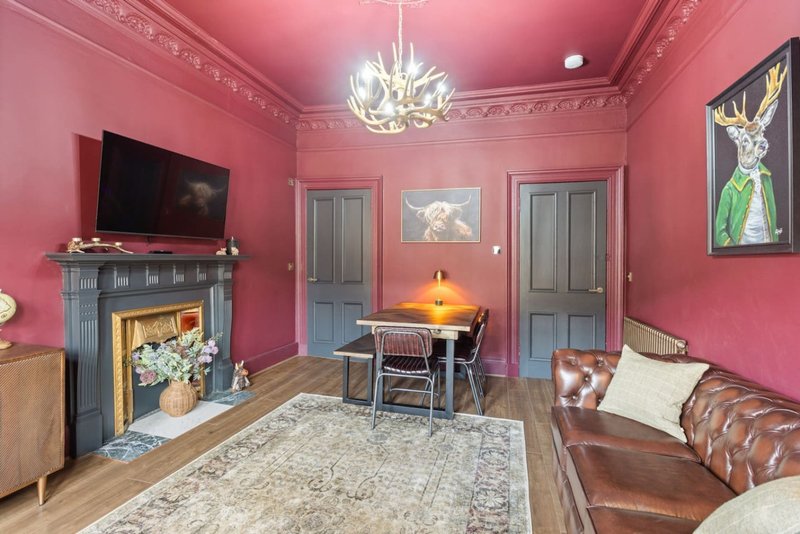 Pink living room with fireplace, leather sofa, TV, chandelier and framed artwork