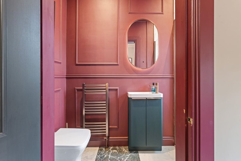 Modern bathroom with pink walls, oval mirror, heated towel rail, dark vanity and white toilet