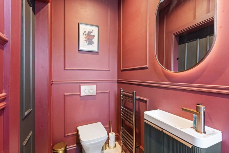 Modern bathroom with pink walls, white sink, toilet, round mirror and framed artwork