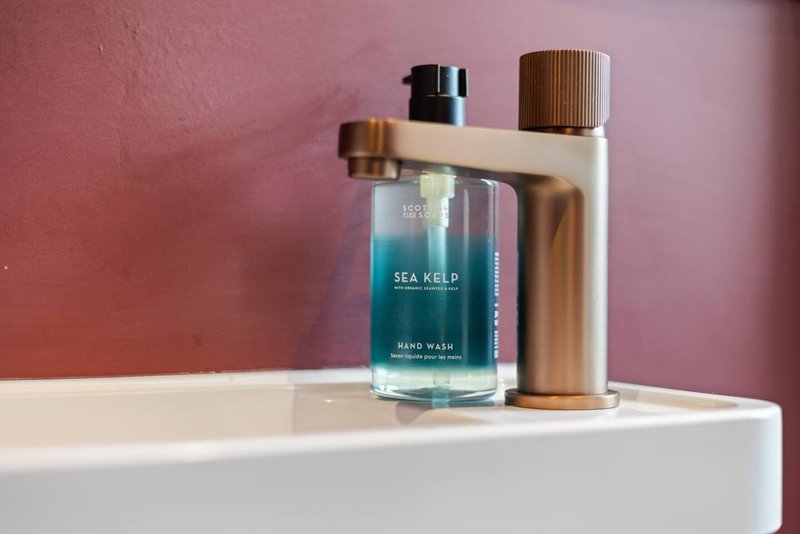 Bathroom counter with sea kelp hand wash bottle and toiletry dispensers against pink wall