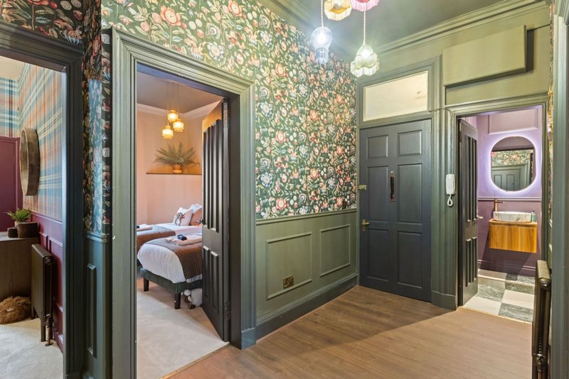 Hallway with floral wallpaper, dark green trim, multiple doorways leading to bedrooms and bathroom