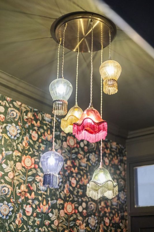 Decorative multi-pendant ceiling light with colorful glass shades hanging in room with floral wallpaper