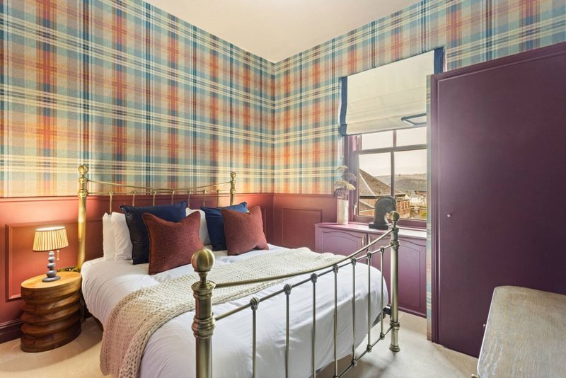 Bedroom with metal bed frame, plaid wallpaper, bedside lamp and purple wardrobe